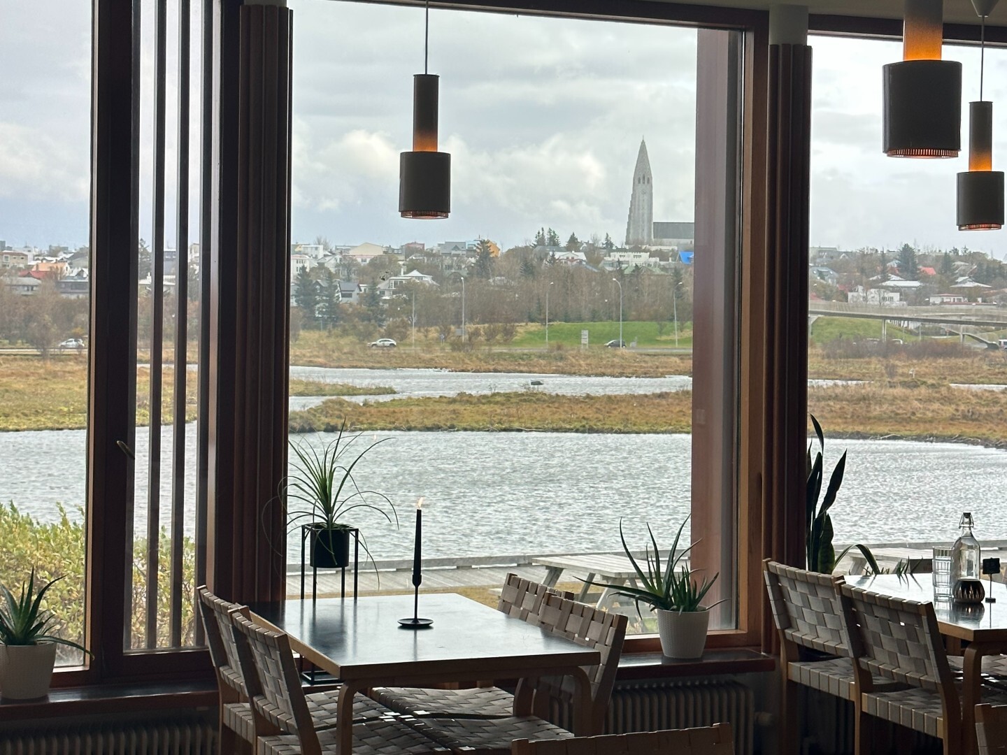 Two empty restaurant tables next to large windows at Nordic House in Reykjavík, with view of water and city in distance