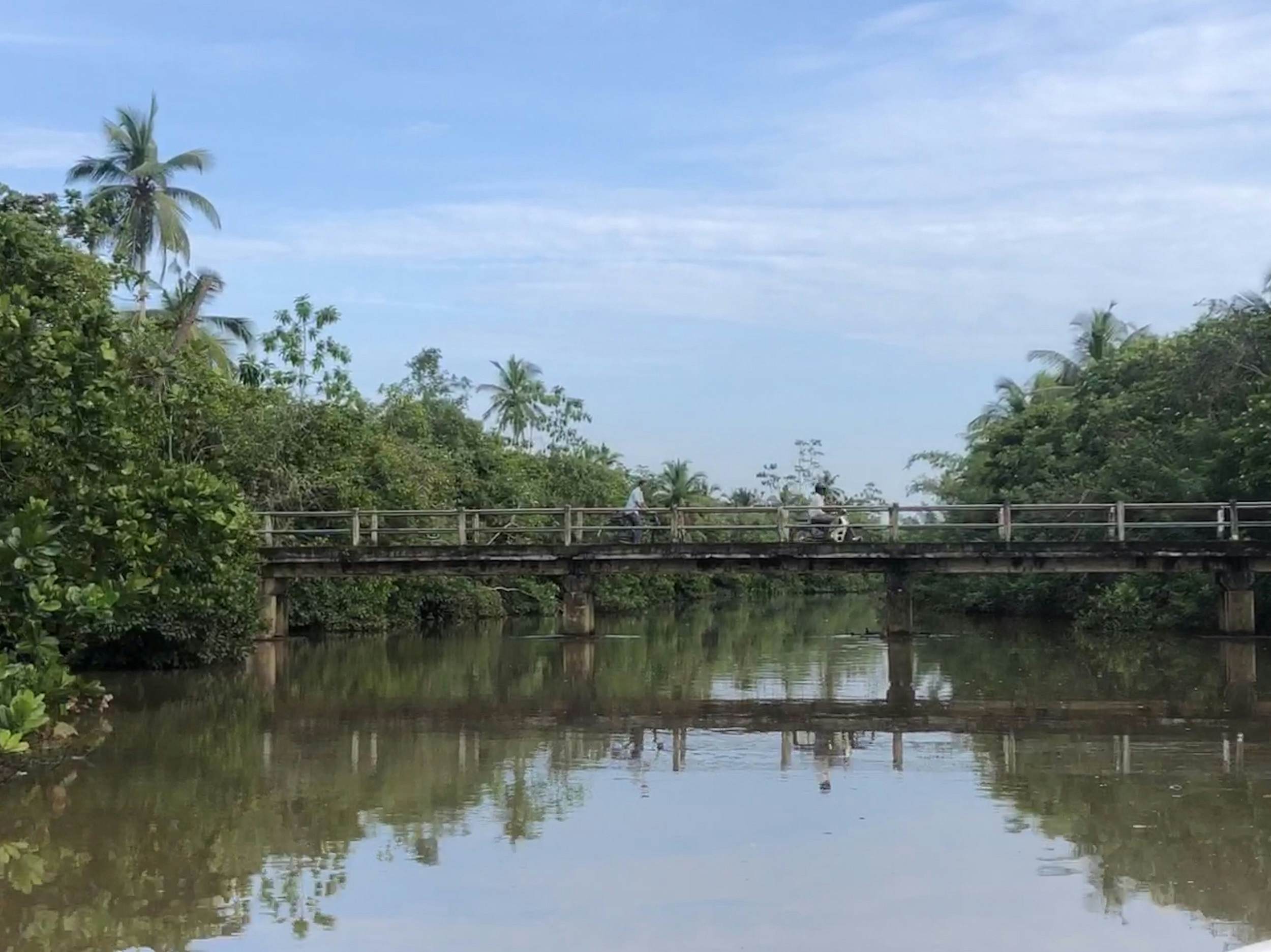 A small pedestrian bridge crosses the Madu River; two people are riding bikes across the cement structure.