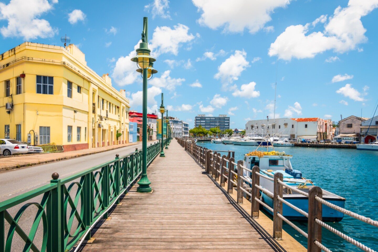 Wooden promenade, with row of green ironwork railing and street lamps beside a body of water