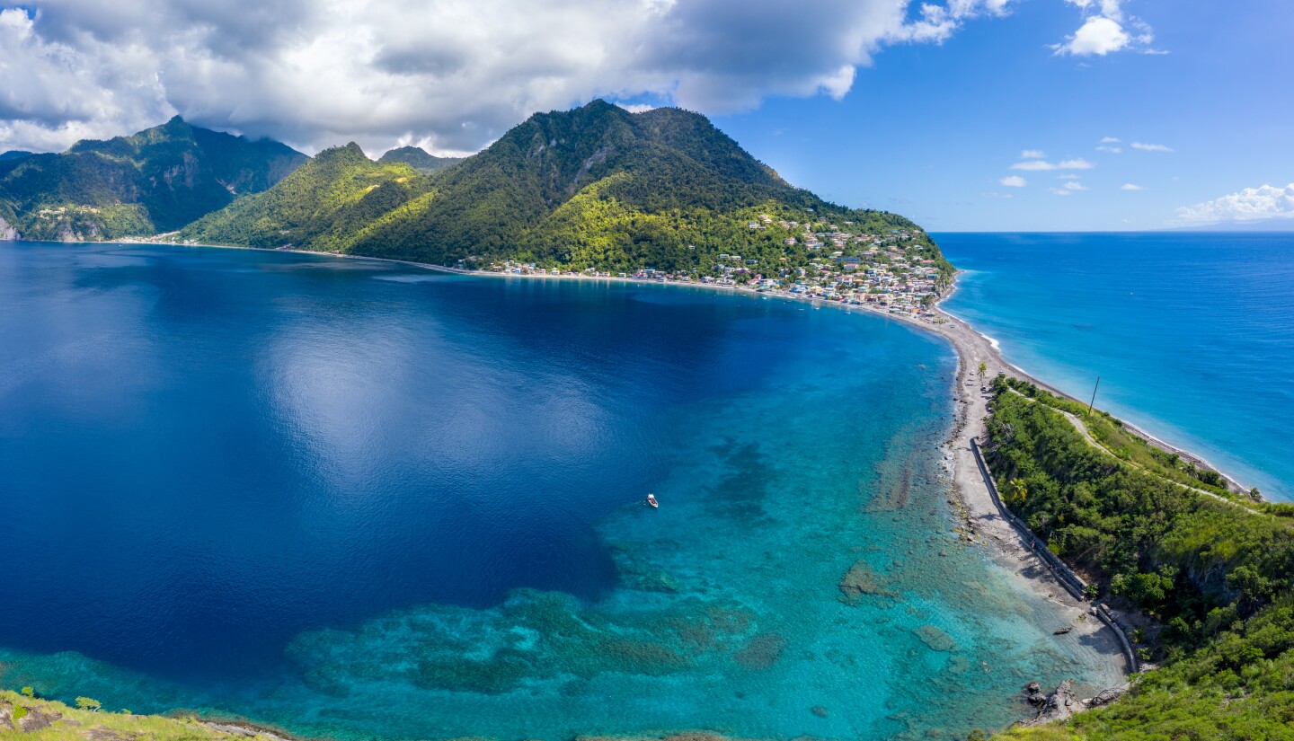 Aerial view of green mountainous land linked by road to small peninsula and surrounded by water