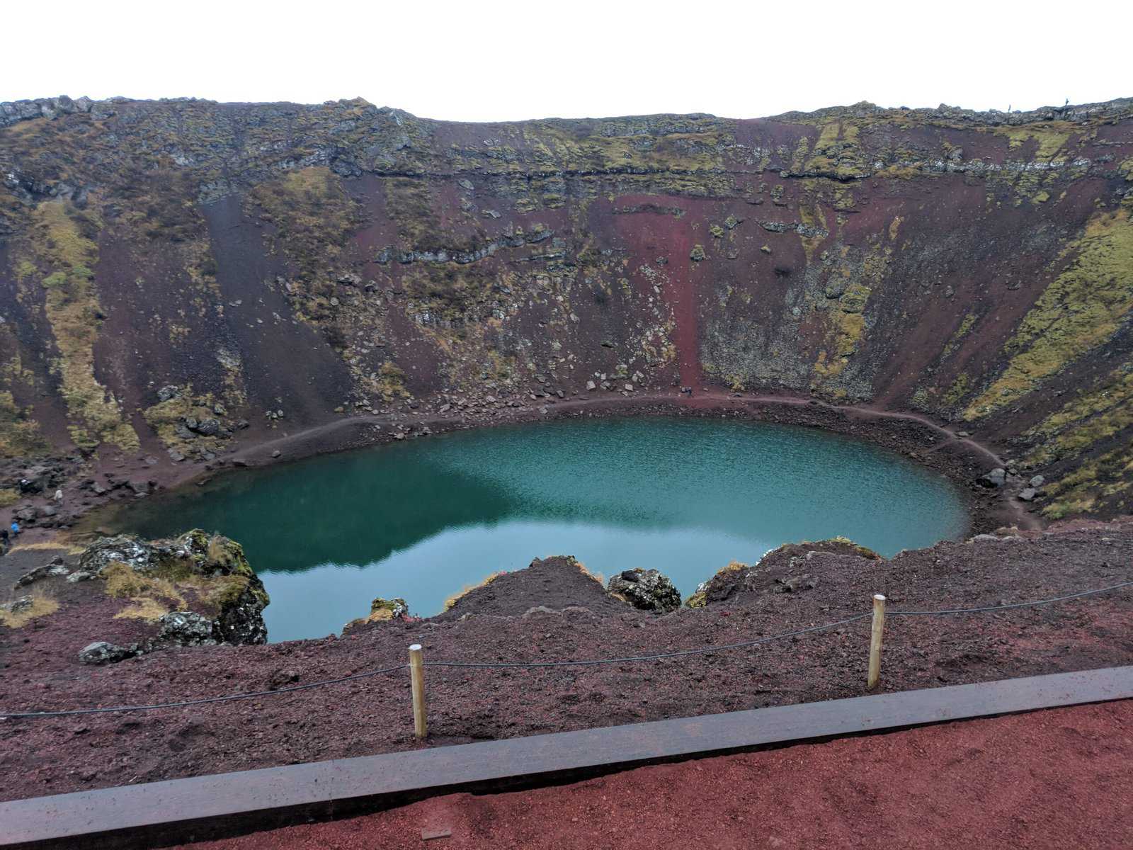 Kerid Crater in Iceland with red and green valley walls sloping down to a bright blue pool in the centre of the crater 