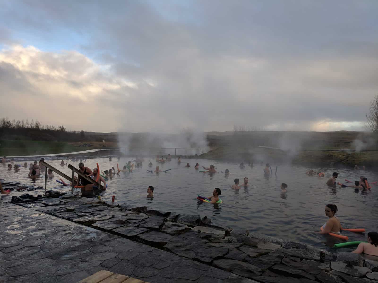 Secret Lagoon in Iceland with people swimming in the hot pool as mist lifts off the water 