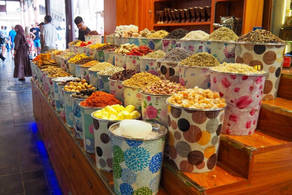 Colorful spice stall at Dubai's Gold Souk with visitors browsing.