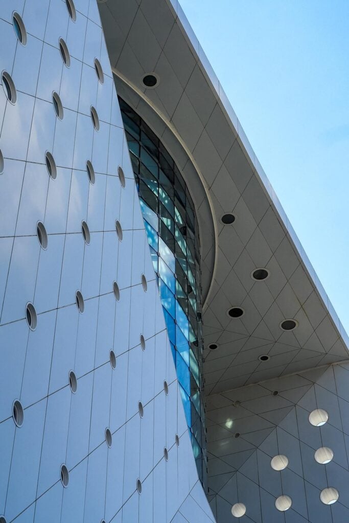 Alt text: The Green Planet Dubai biodome, eco-friendly architectural marvel with circular fixtures and curved glass window against blue sky.