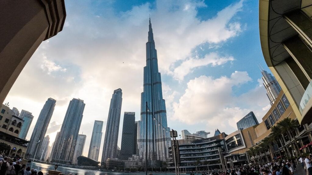 Wide-angle shot of Burj Khalifa towering above downtown Dubai at sunset with clouds in the sky, reflecting the city's dynamic mix of modern architecture and leisure attractions.