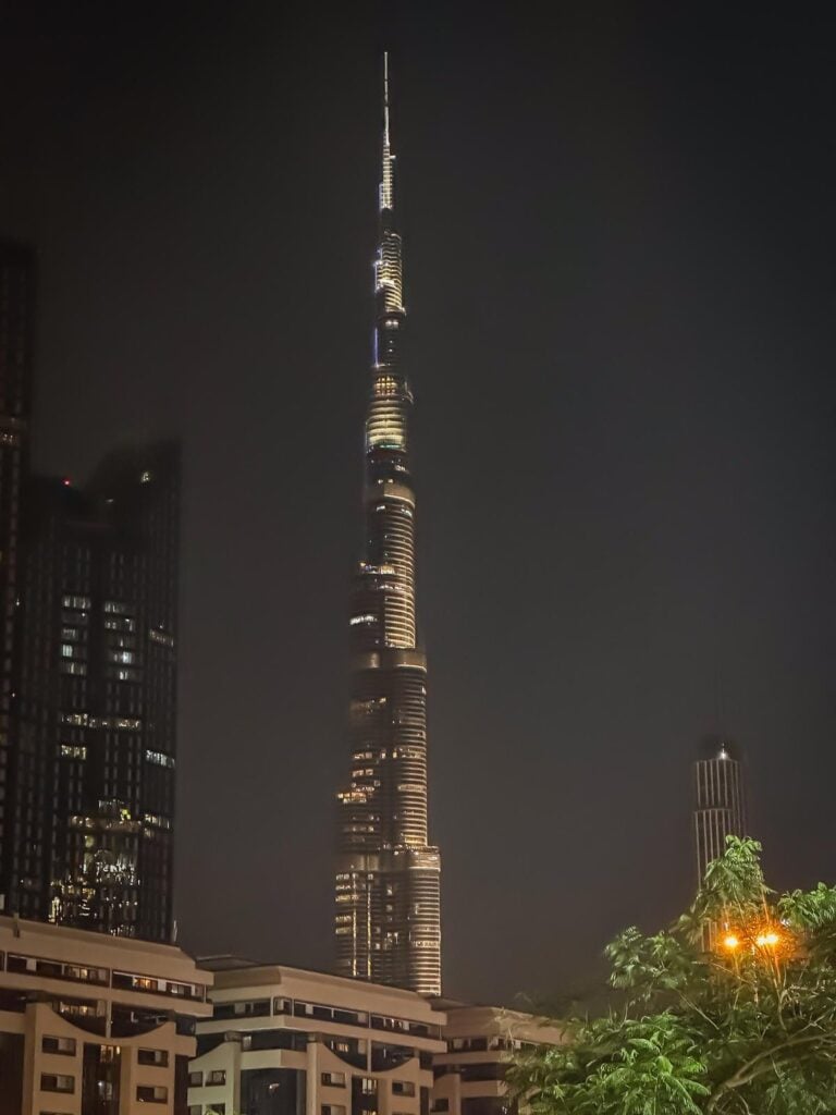 Illuminated Burj Khalifa at night with surrounding buildings, showcasing Dubai's iconic skyline and architectural grandeur.