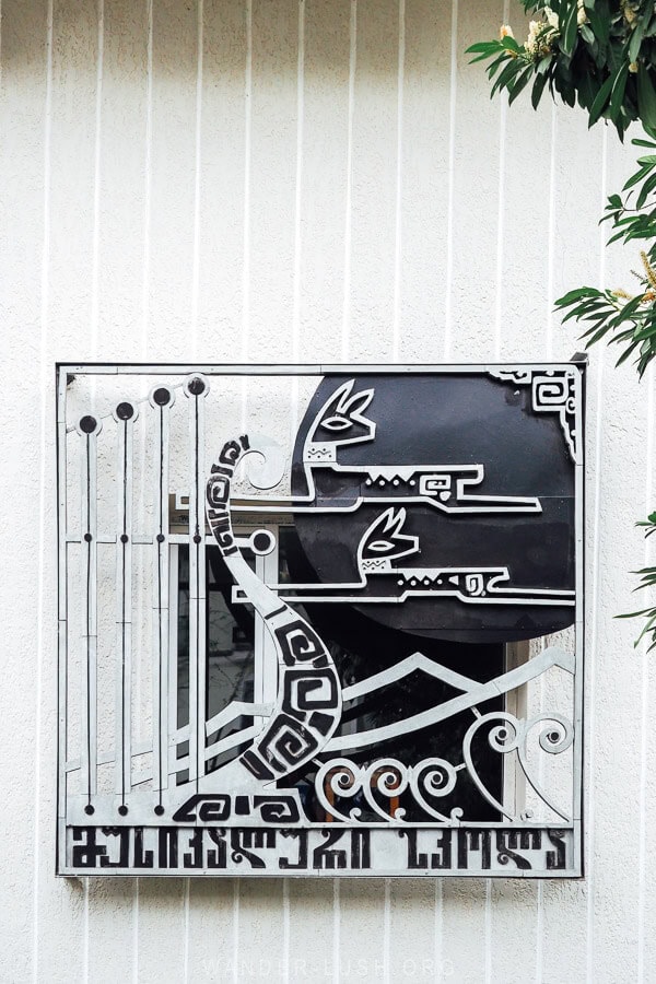 A decorative metal plate on the front of the music school in Gurjaani, with deer decorations and Georgian text.