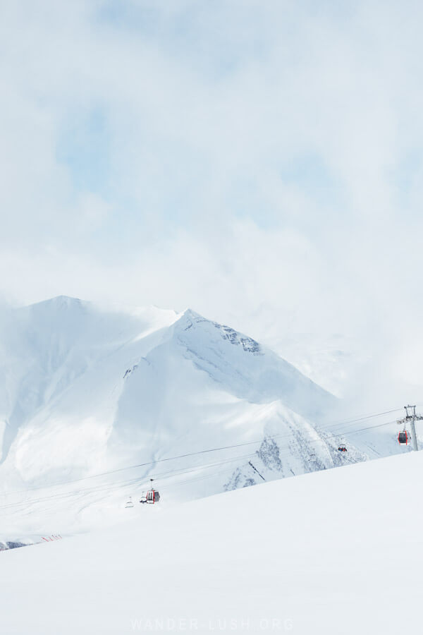 A mountain with red and black gondolas running below it at the ski resort in Gudauri, Georgia.