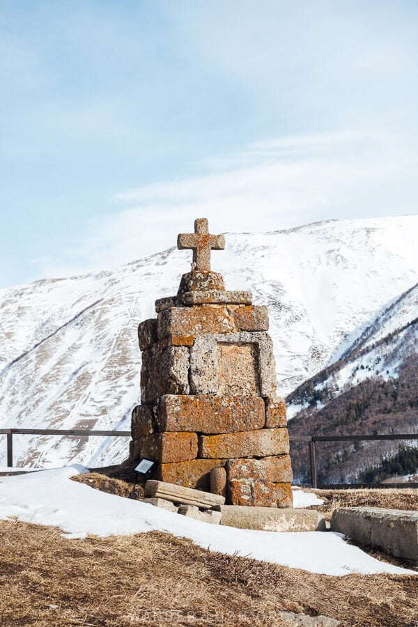 A stone cross on snowy ground overlooking the mountains at Sioni Basilica near Gudauri.