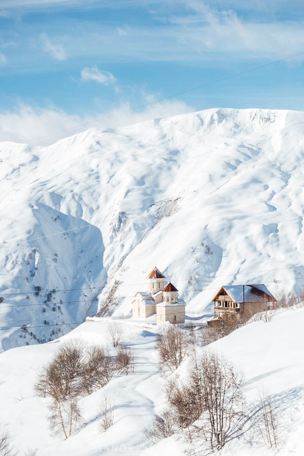 A modern church in Gudauri seen from afar against a backdrop of snowy mountains.