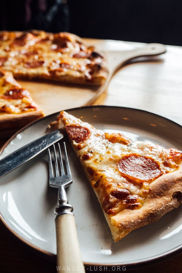 A slice of pizza on a white plate on a wooden table at Gudauri restaurant near the ski lifts.