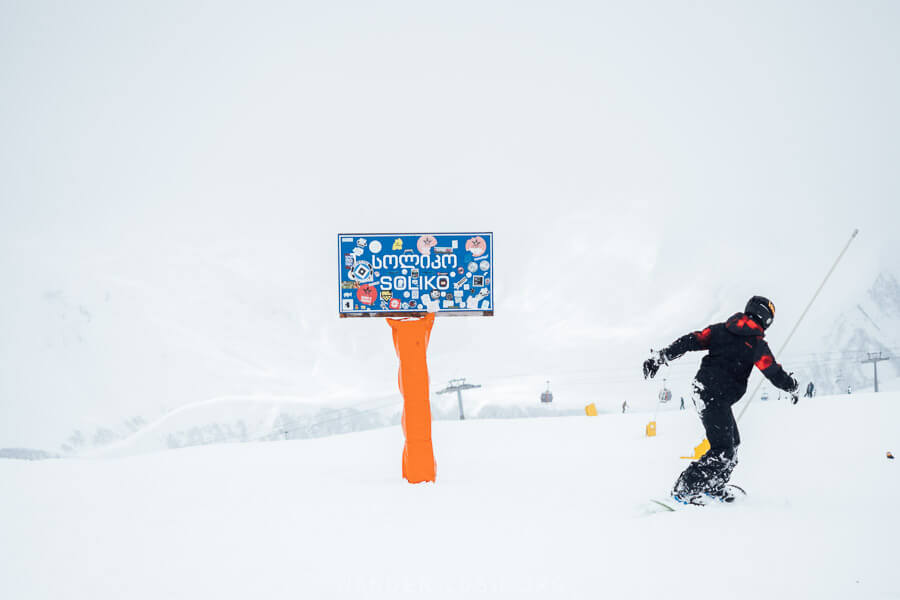 A man snowboards past a sign at Gudauri ski resort for the Soliko lift.