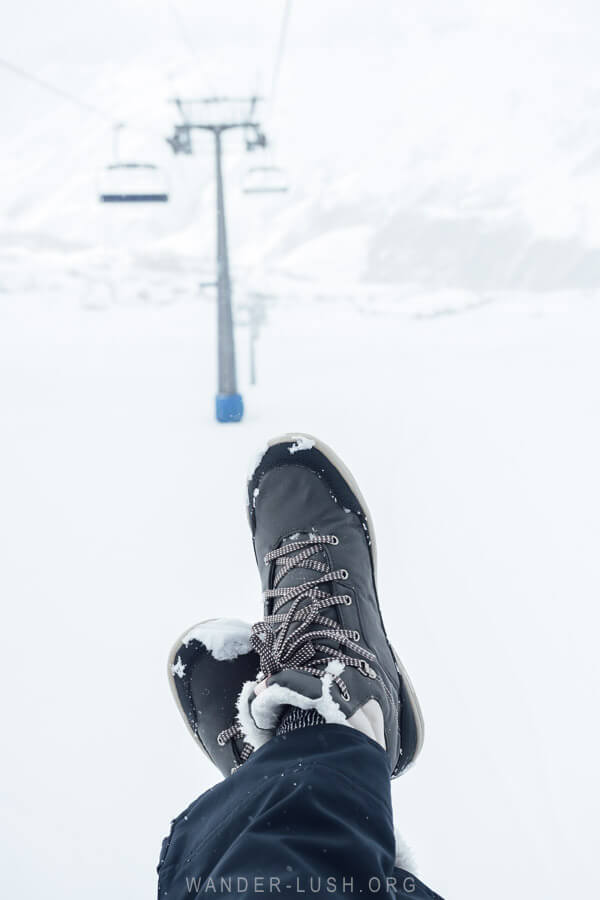 A woman with crossed legs wearing snow shoes on a chairlift in Gudauri.