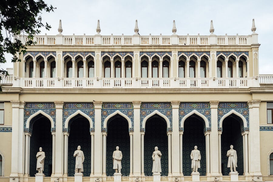 Six statues of famous writers and poets standing in arched openings on the facade of the Nizami Museum of Azerbaijani Literature.