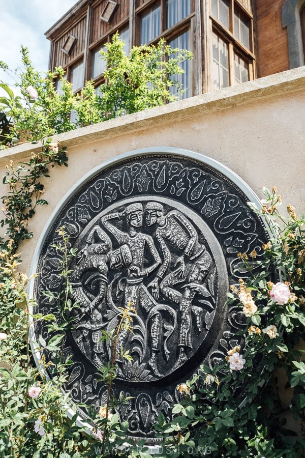 A decorative medallion depicting oil field workers in front of a heritage wooden facade in Baku.