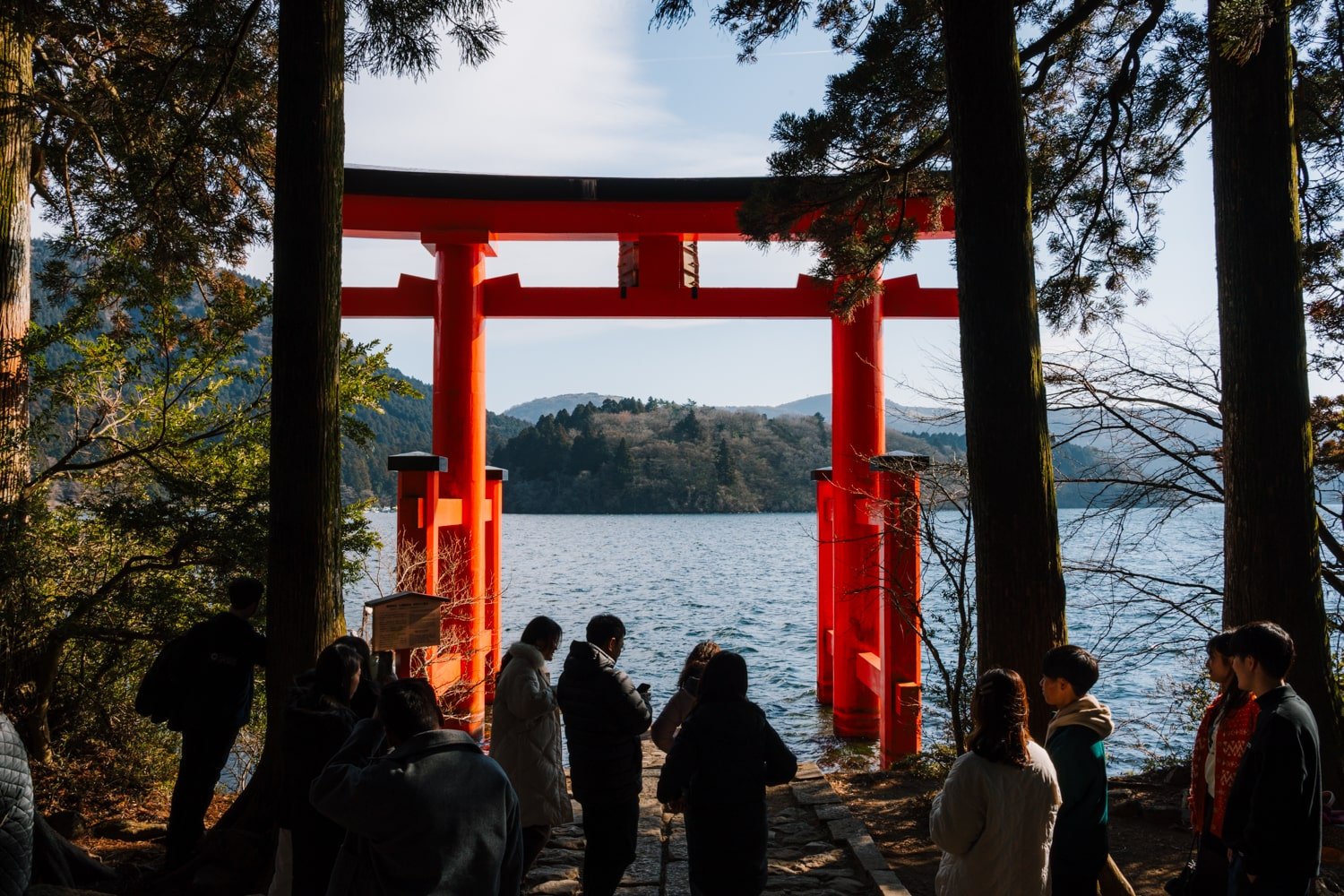 Tourists line up to take a photo of the red Hakone Shrine Torii gate rising out of the water at Lake Ashi in Hakone, Japan.