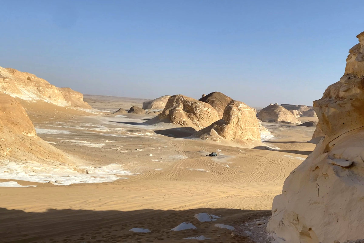 The white desert in Egypt is filled with rock formations and splatters of white sand on top of beige sand. 