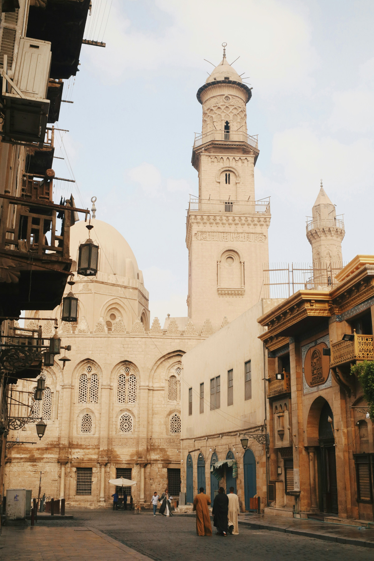 The tall minaret and dome of the Qalawun complex loom over a small sidestreet.