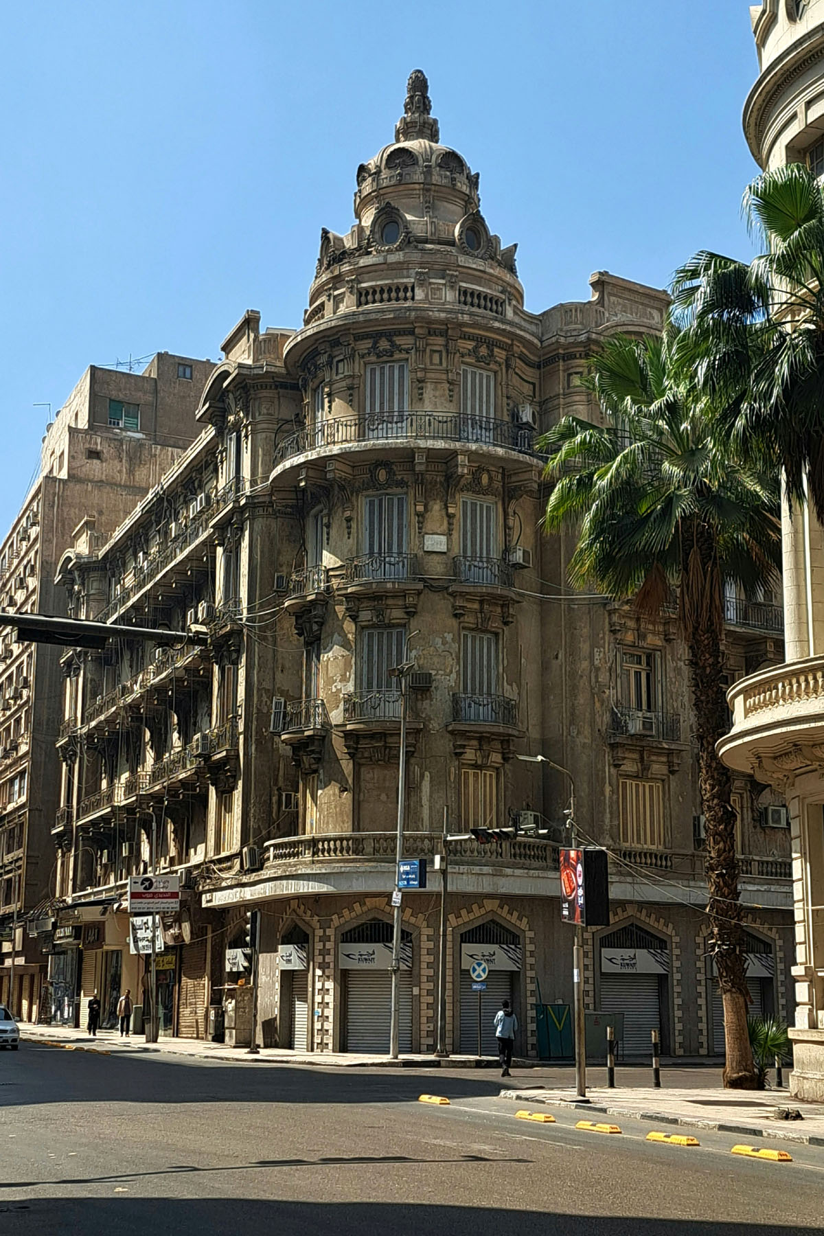 A tall ornate building stands on a corner of downtown Cairo. It has intricate architecture and balconies. 