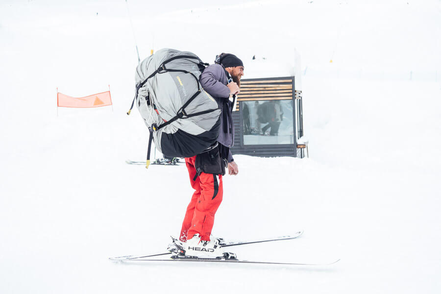 A man carrying a paragliding backpack on skis in Gudauri, Georgia.