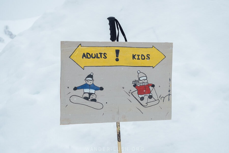 A sign in Gudauri ski resort pointing to adults' and kids' ski areas.