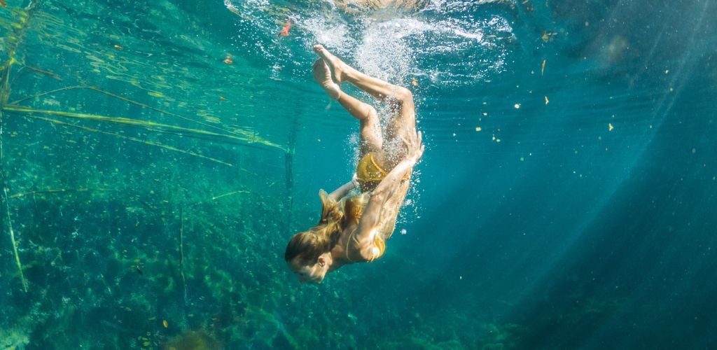 A woman swimming deep in a cenote underwater view.