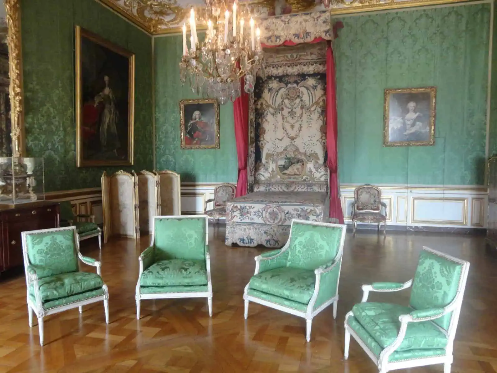 Bedroom with a chandelier, bed and four big green chairs in the Palace of Versailles, France