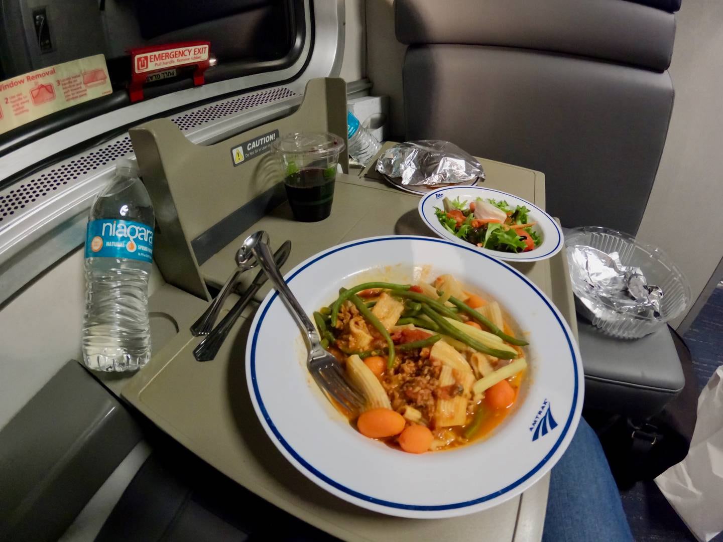 a bowl of pasta, a side salad and a plastic cup of wine on a private Amtrak room table