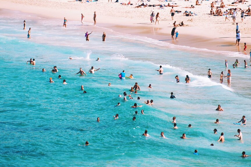 Busy Australian beach with people swimming and sunbaking showing some of the benefits of life in Australia.