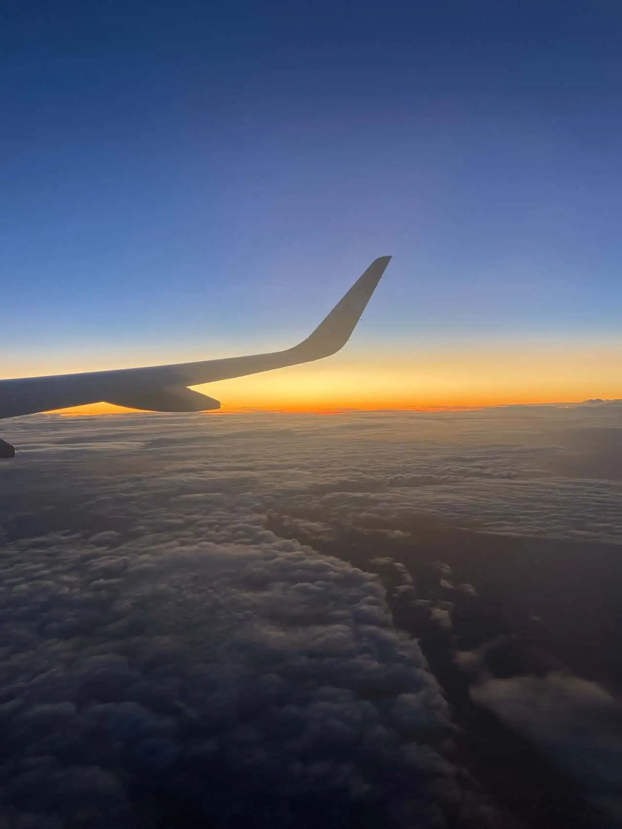 Wing of the plane with the sun setting behind it on a flight from Auckland to Queenstown during our 14 day itinerary for New Zealand