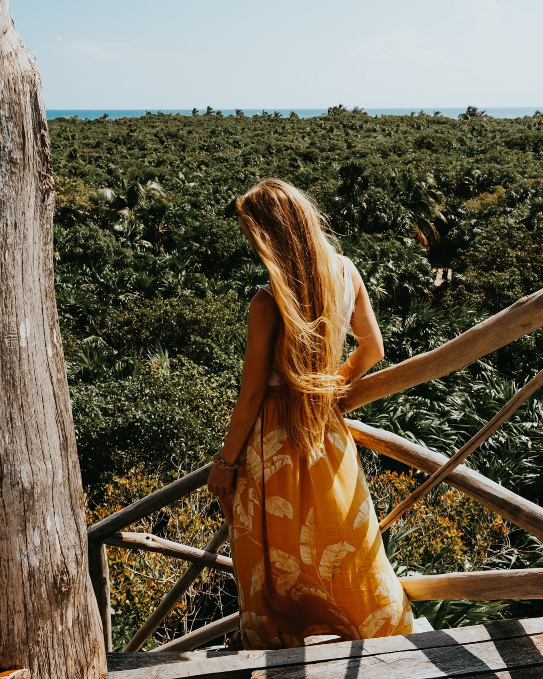 Blonde female traveler standing on Sian Ka'an watch tower overlooking jungle.