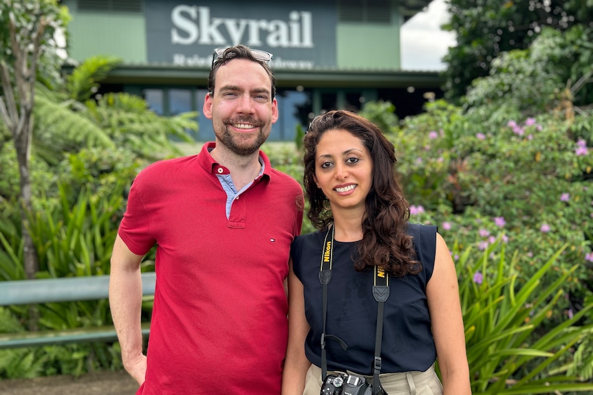 A young man and woman pose for a photo infront of some bushes