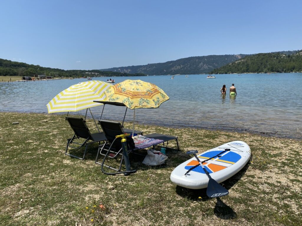 A pair of beach chairs, umbrellas, and a paddleboard on the shores of Gorges du Verdon and Lac de Sainte Croix in France