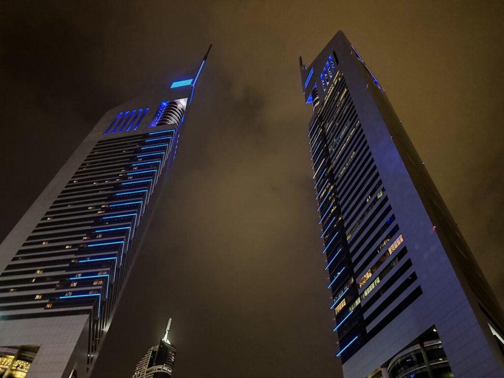 The Emirates Towers in Dubai at night, with blue lighting accents against the dark sky.