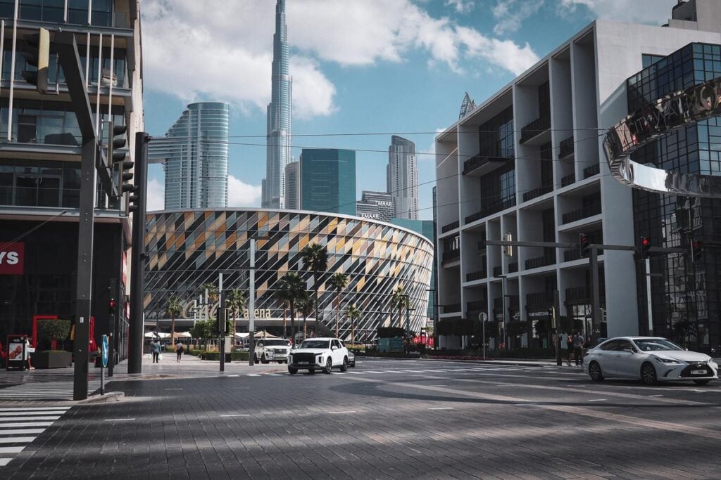 A dynamic street view of City Walk in Dubai, featuring traffic, the Coca-Cola Arena, and the silhouette of Burj Khalifa against a clear blue sky.