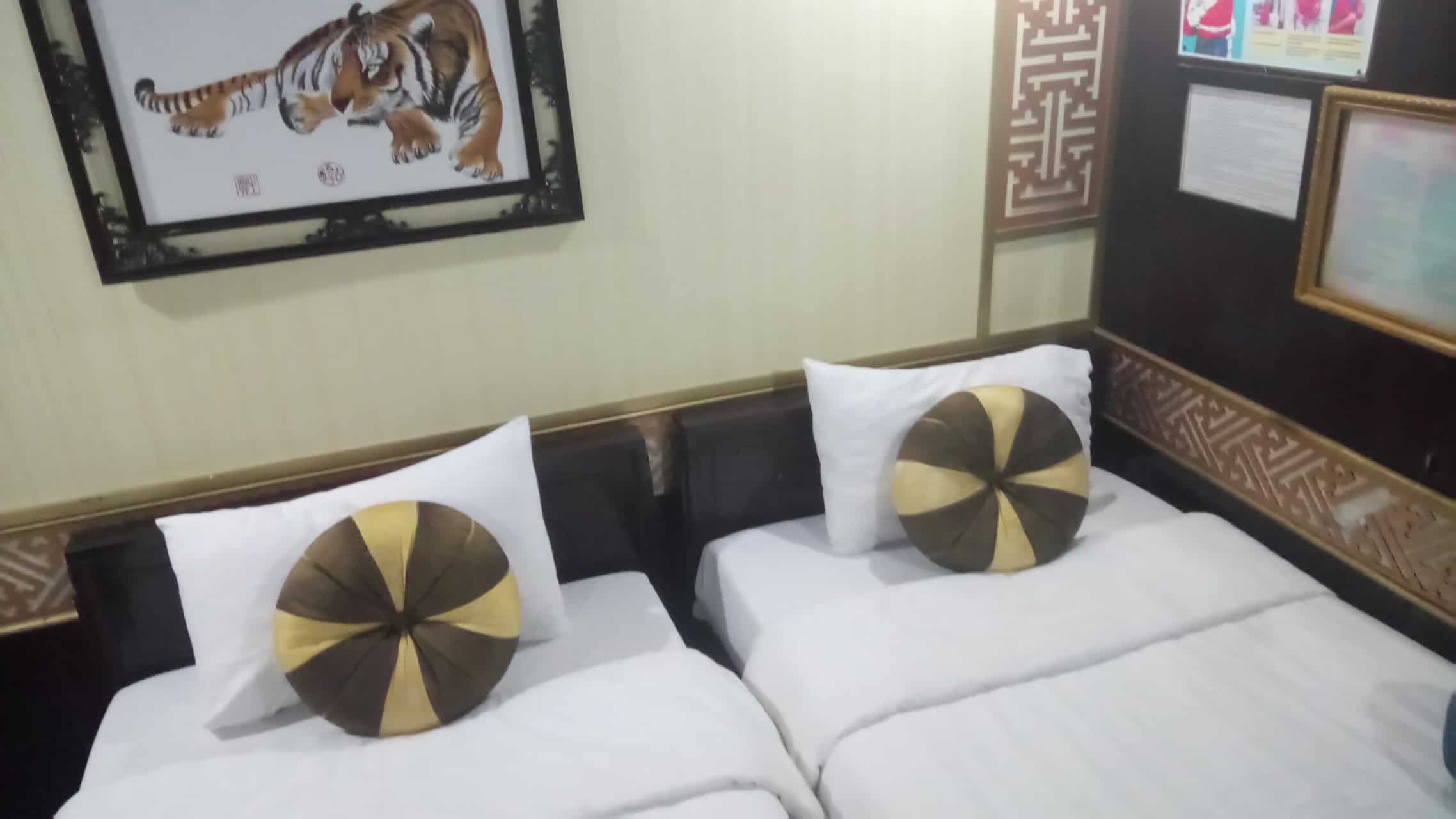 Cabin on our Halong Bay cruise in Vietnam with two twin beds next to one another, each with two pillows, and a tiger painting on the wall behind