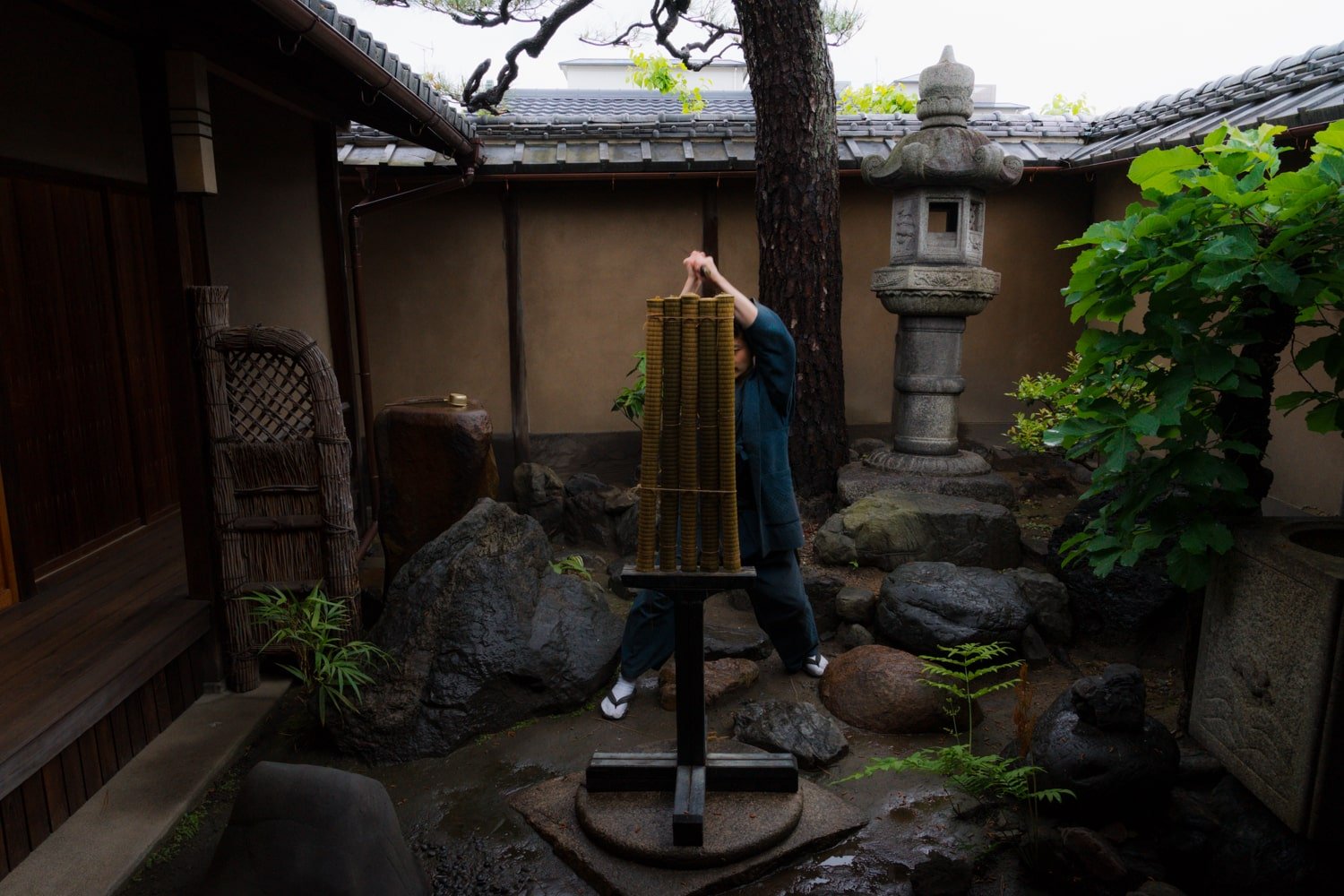 A katana sword master prepares to slice through 5 rolled tatami mats in a Japanese garden.