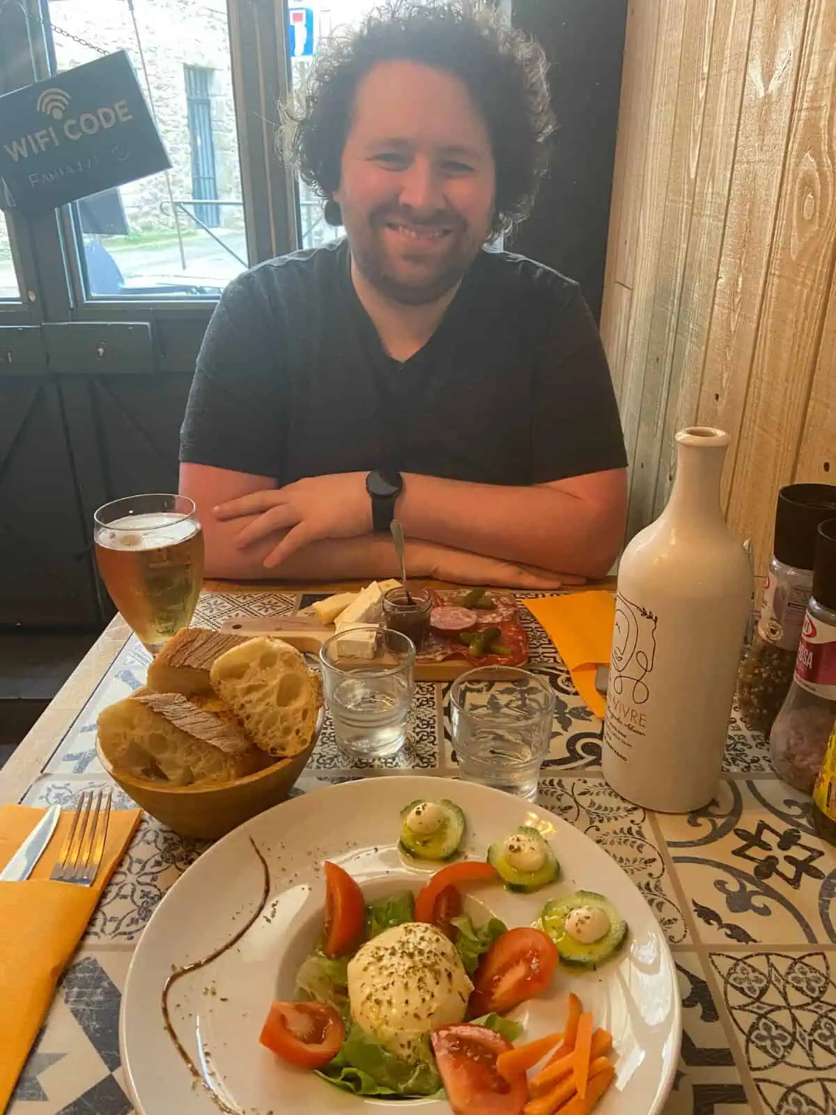 Colin eating lunch at a restaurant in Carcassonne, France. In front of him is a chacuterie board and pint of beer. 