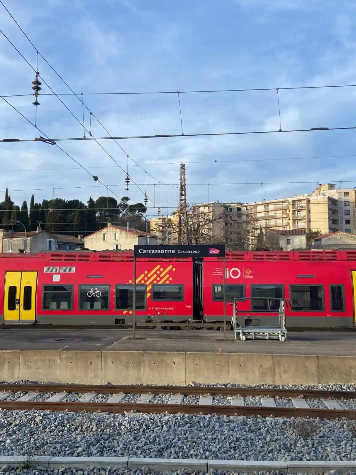 Carcassonne train station in France with red train cars in the background on the tracks