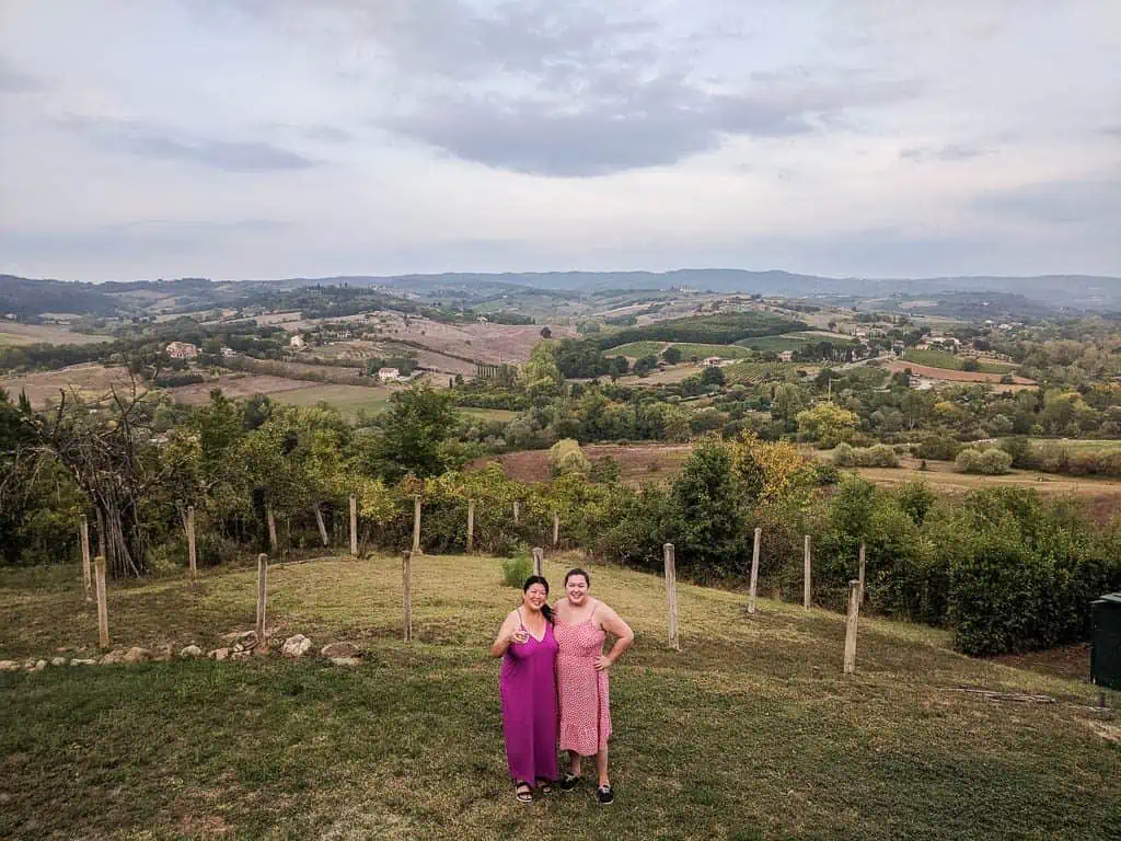 Riana and her mom posing on a field in Tuscany with rolling hills of green and brown behind them