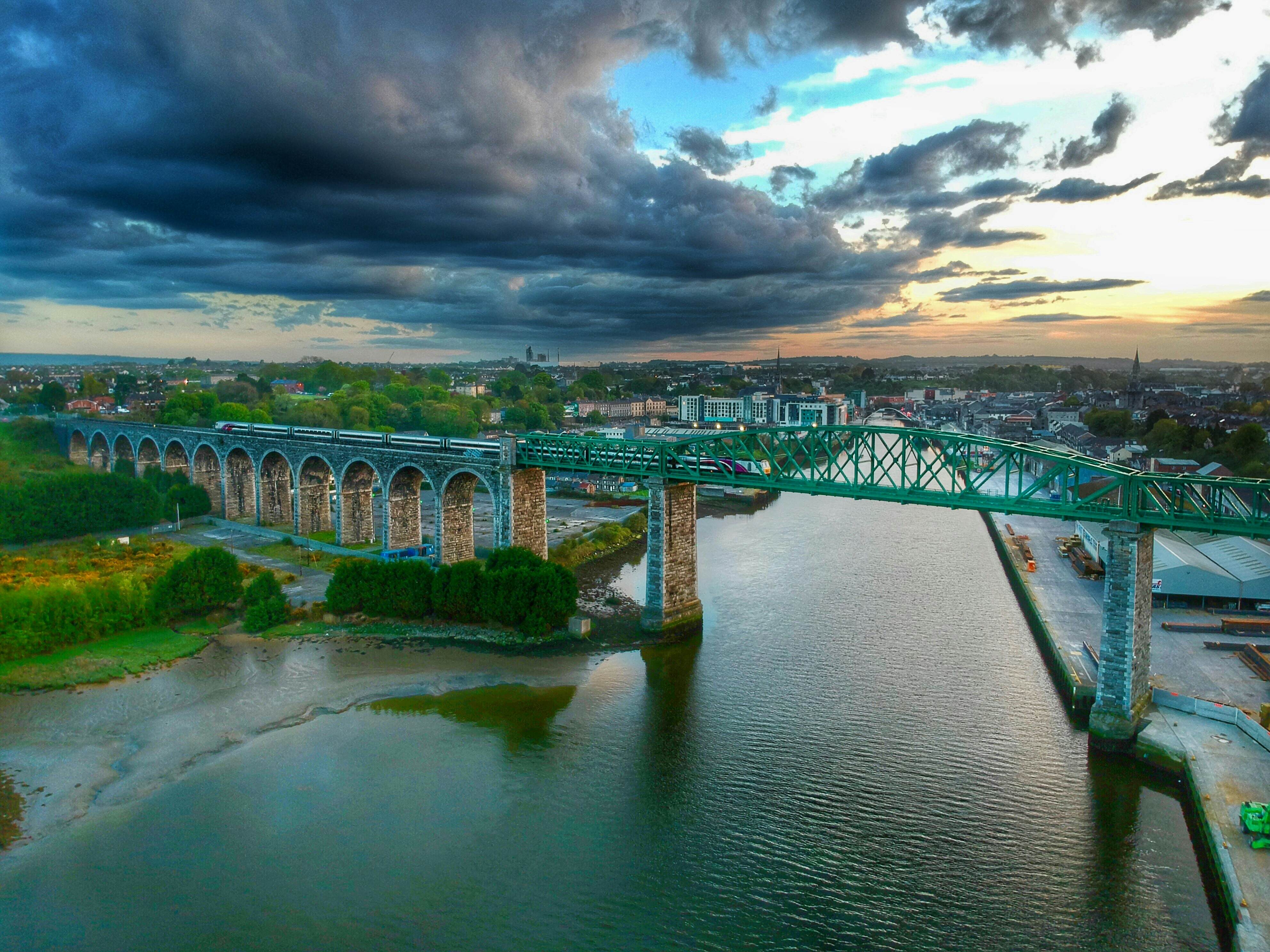 A train crosses a viaduct below a dramatic cloudy sky