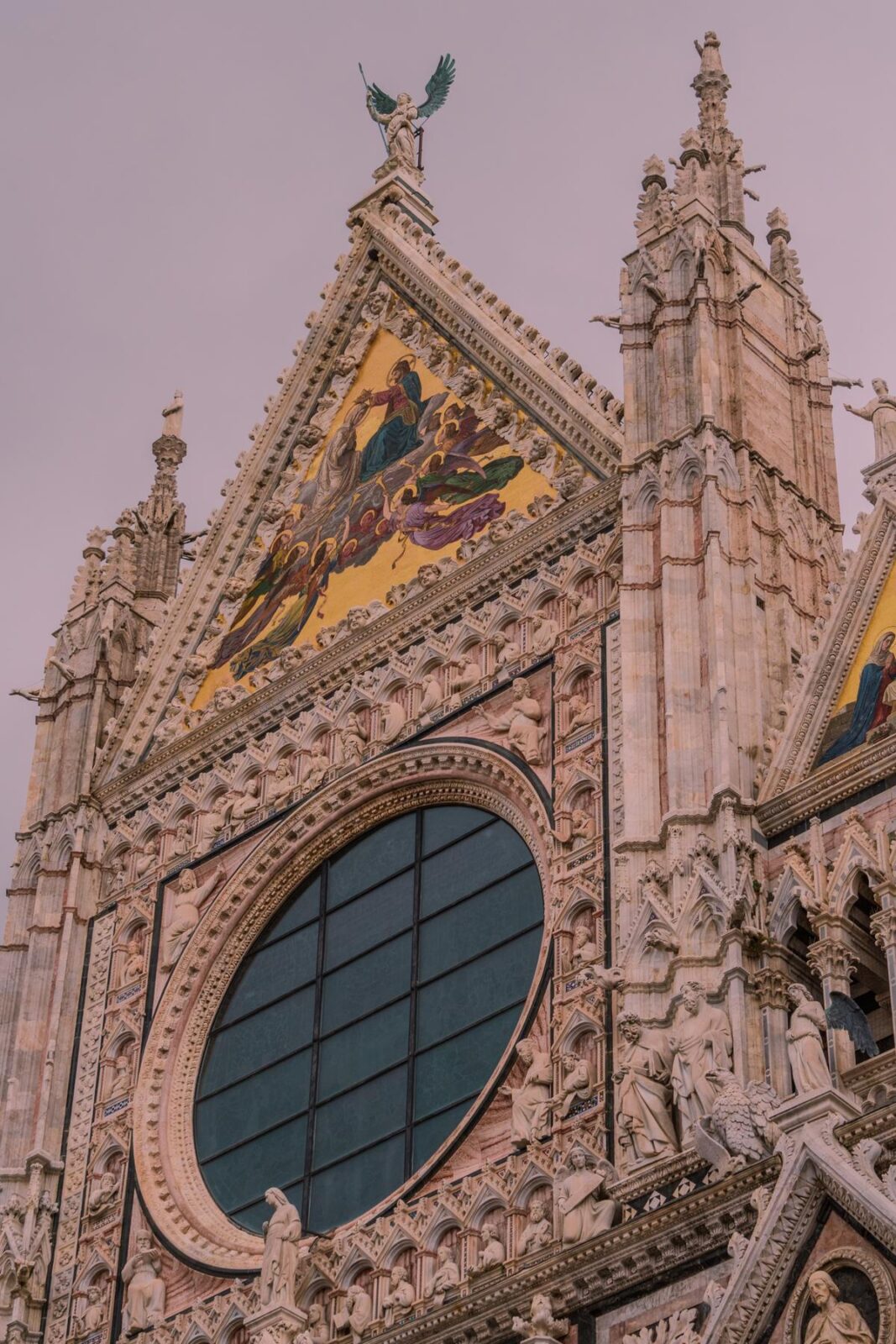 Siena Cathedral Gothic facade, rose window, and sculptures against moody sky