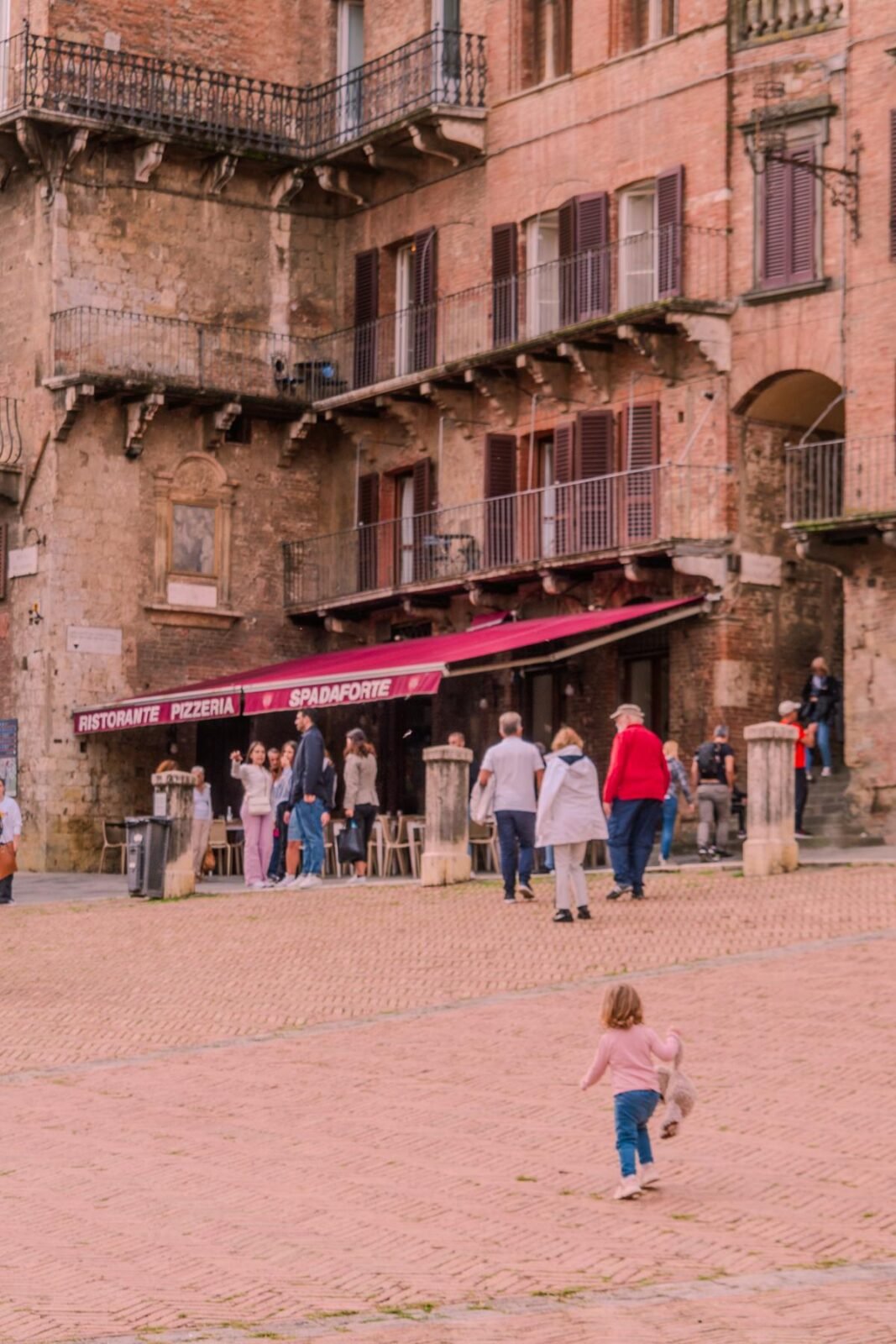 Visitors on cobblestone street amidst Siena's historic Tuscan architecture