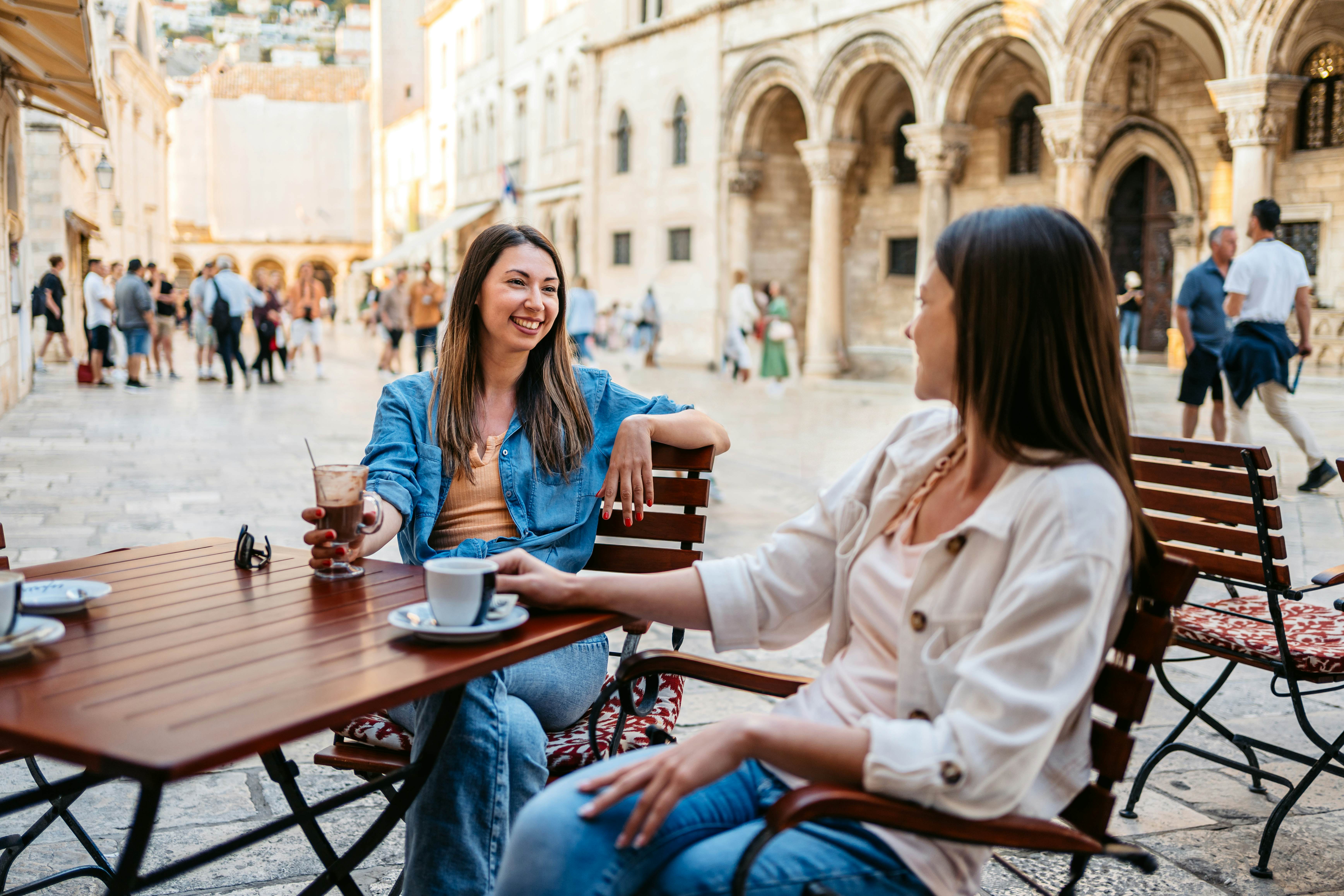 Two young female friends drinking coffee in a sidewalk café in Dubrovnik, Croatia