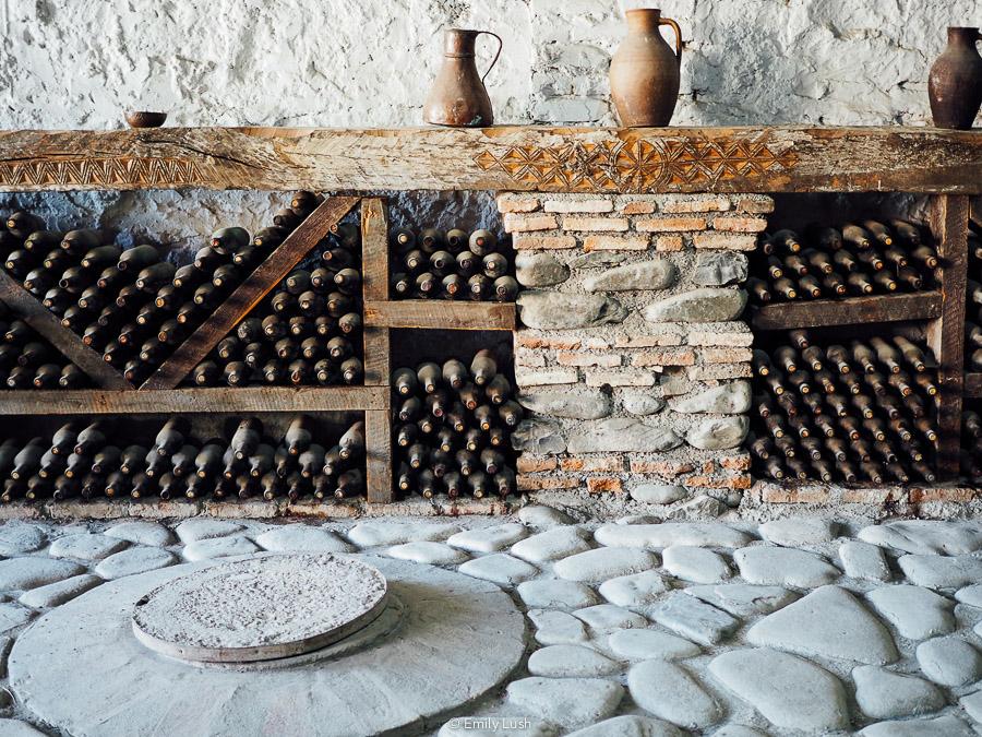 A stone wine cellar with stacks of bottles and old clay jugs.
