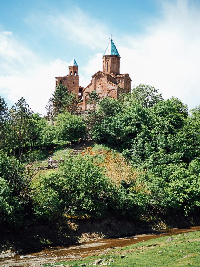 Gremi Church in Kakheti, a turquoise topped stone church on the crest of a green hill.