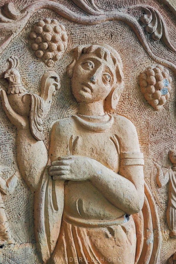 Details on a Soviet-era sculpture in Kakheti showing a woman holding a bird amongst grape vines.