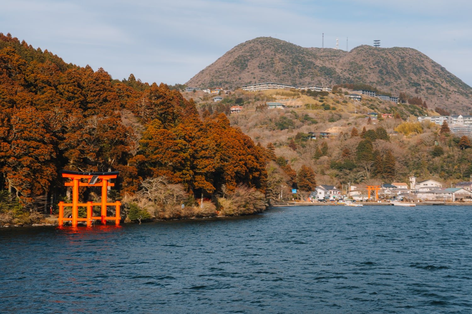 The vermillion Hakone Shrine Torii gate rising out of the water at Lake Ashi with a view of Motohakone-ko, Japan.