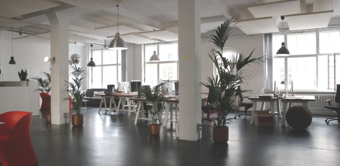 open-planned office space example, multiple desks and seating areas with potted indoor plants 