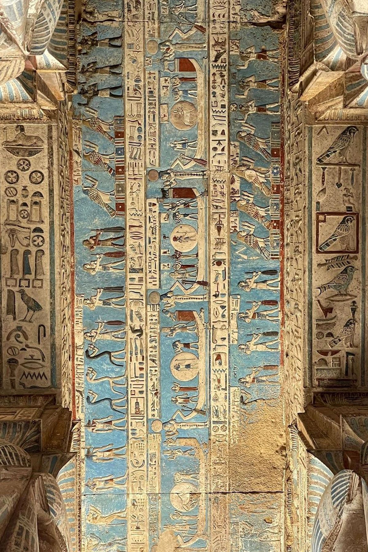 A view looking up at the ceiling of the Dendera Temple in Egypt shows hieroglyphs in striking blue colors. 